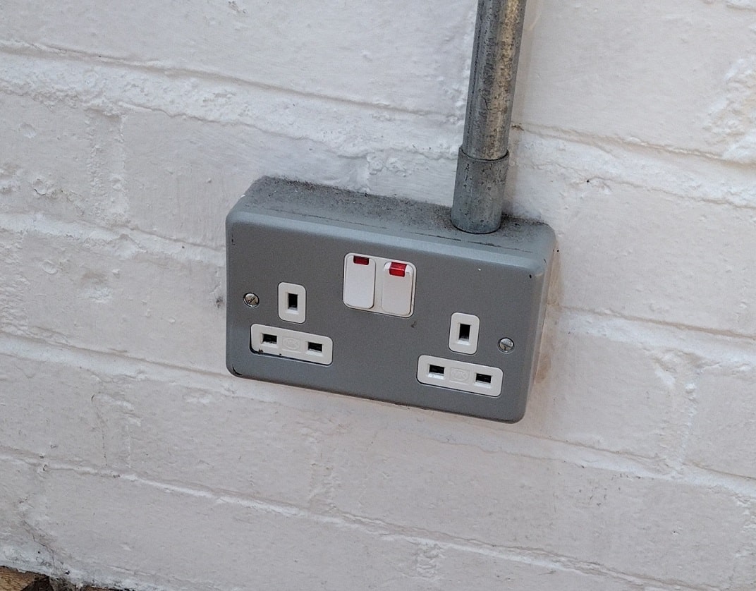 wall-mounted metal double socket outlet with plastic portion partially pushed into the box